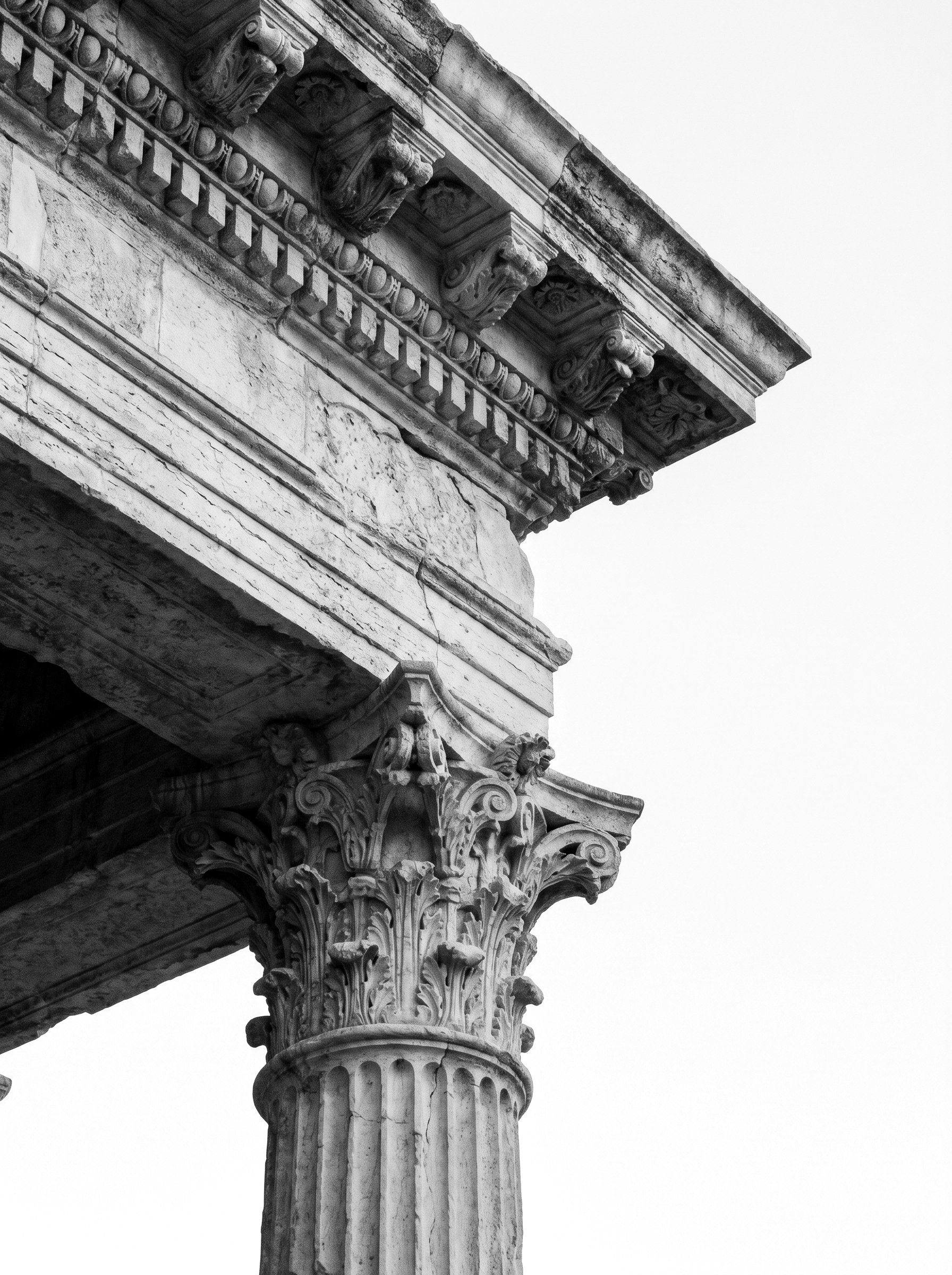 A classical column capital and entablature, photographed from below against an empty sky.